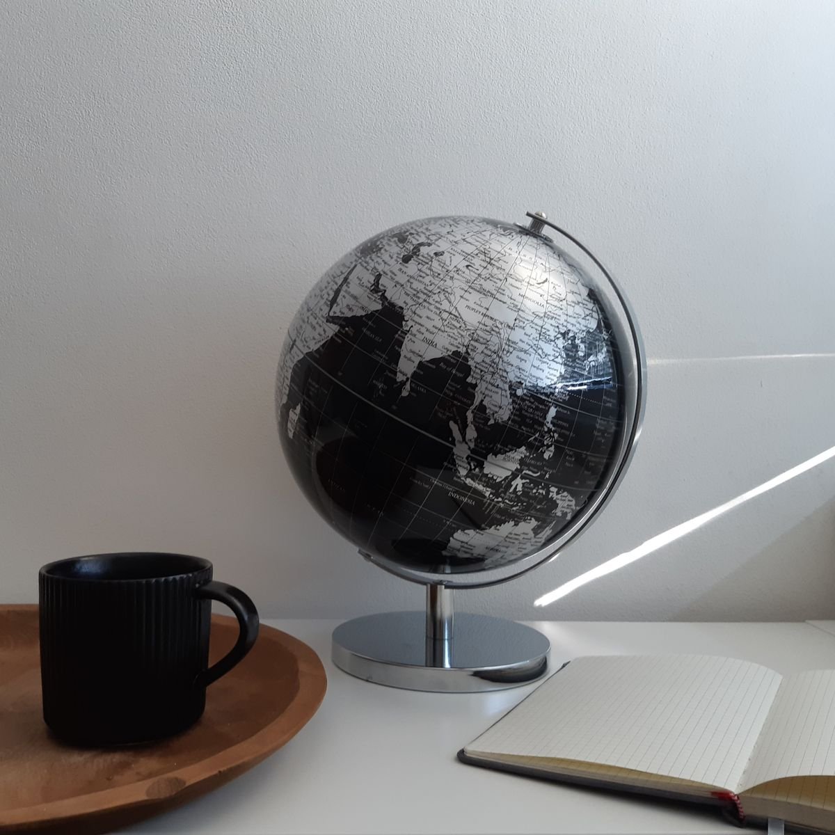 A desk with a globe, notebook, and coffee mug