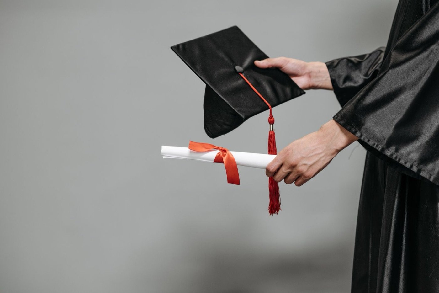 A graduate holding a diploma and mortarboard cap